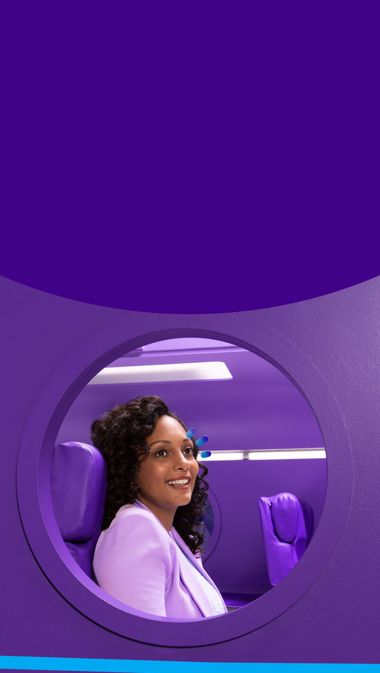 A woman sitting in a purple seat looking out the window of an airplane with purple walls