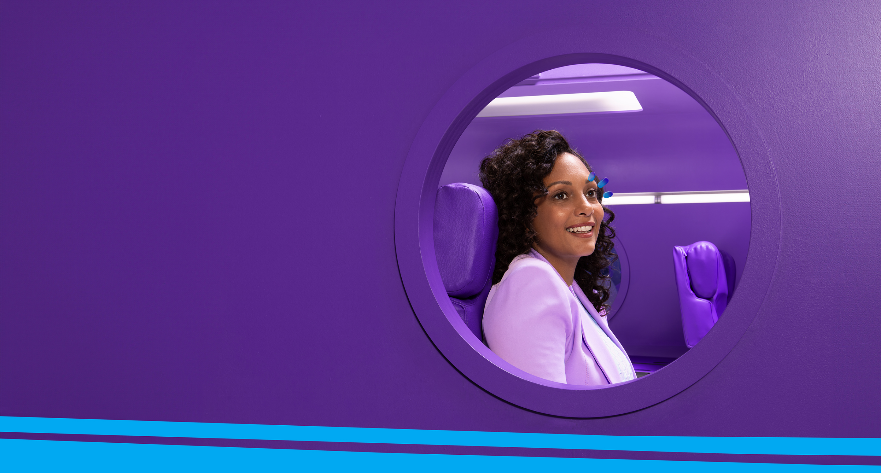 A woman sitting in a purple seat looking out the window of an airplane with purple walls