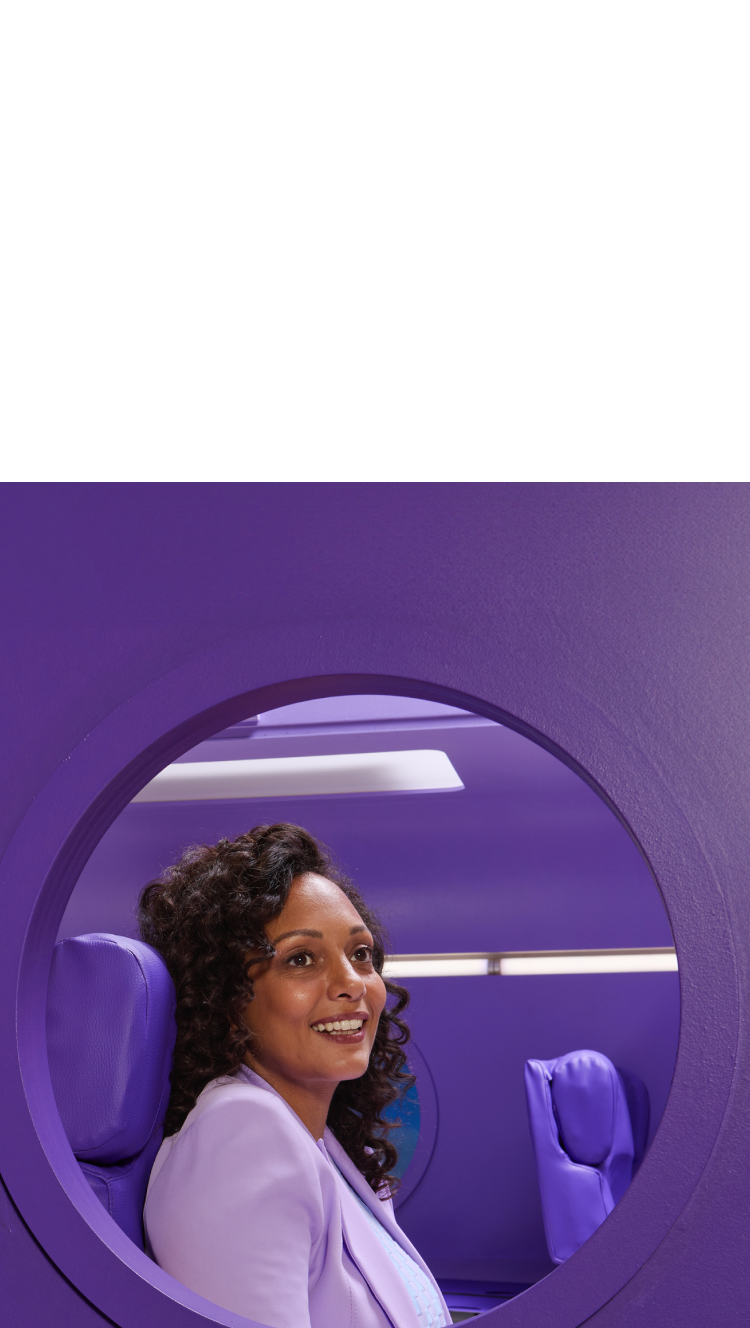 A woman sitting in a purple seat looking out the window of an airplane with purple walls