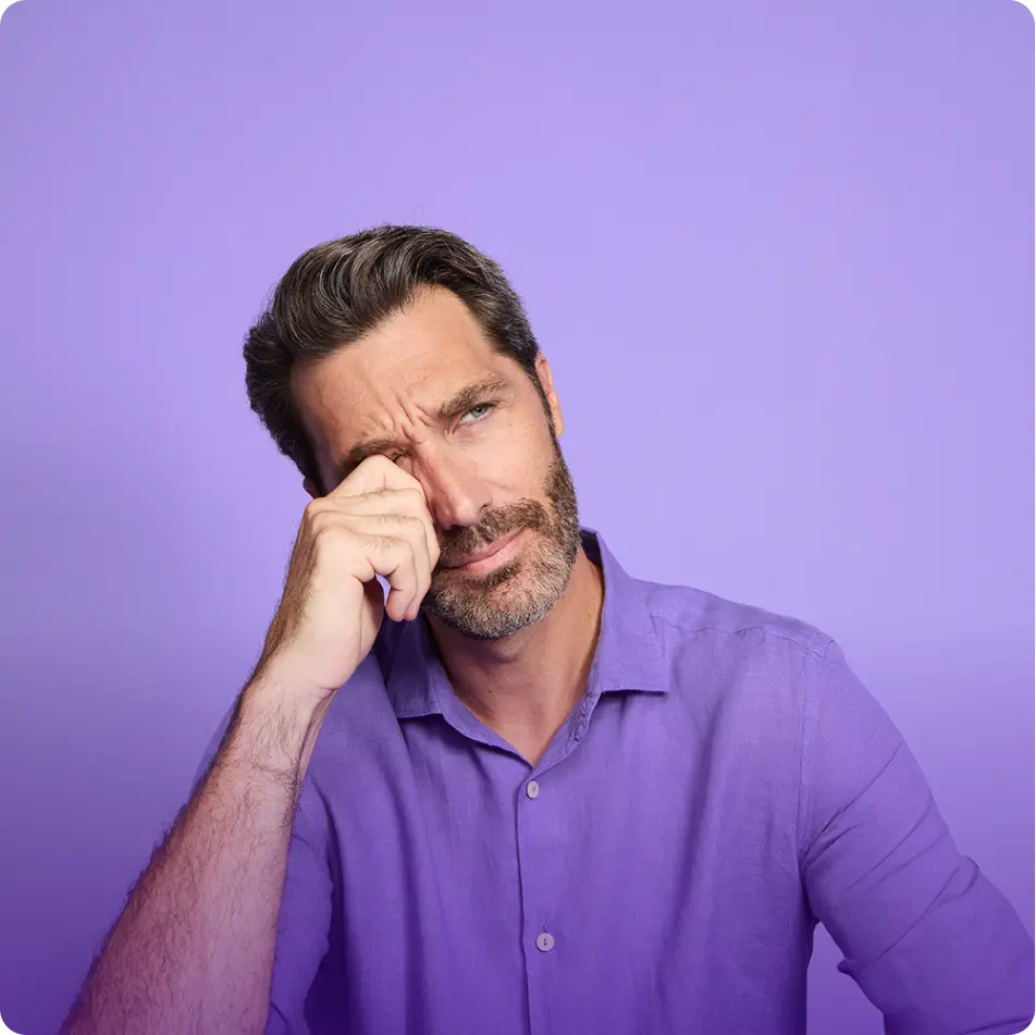 Man in purple shirt rubbing at his right eye